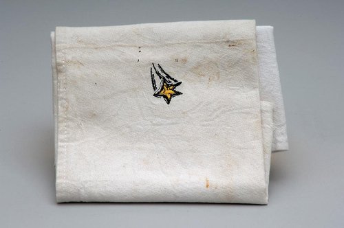 A clothed restaurant napkin. It white but dirty with stains and has wrinkles. At the corner is a small shooting yellow star. 