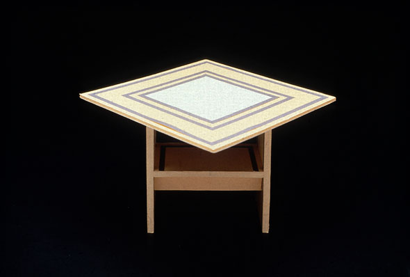 Photograph of a striped table with a chair visible underneath it