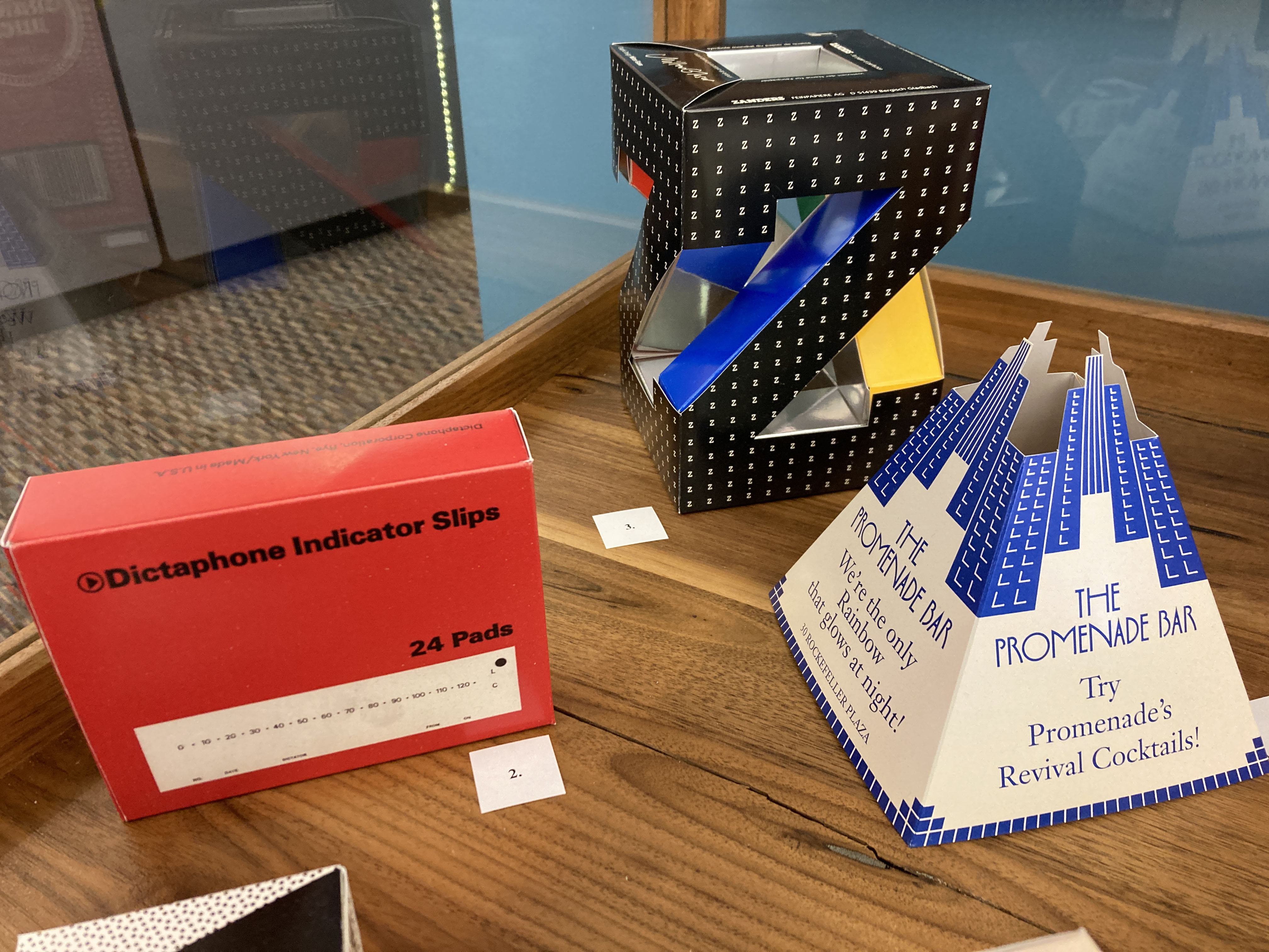a red box for dictaphone indicator slips, a pyramidal table tent for "the Promenade Bar," and a large cubic Z for "Zanders"