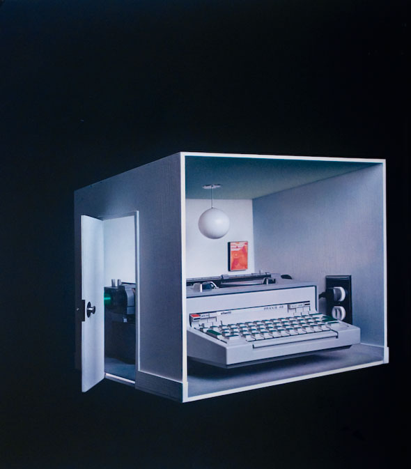 A model of a white room in a dark space, it's filled with tiny furniture but an oversized white typewriter takes up most of the space.