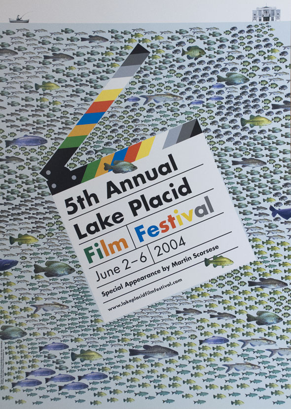 A poster of an opened clapperboard with title "5th Annual Lake Placid Film Festival", in front of a light blue background filled with fish. A person fishes in a rowing boat above to the left, and an image of a house on the right,