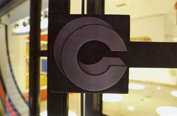 A close up photo of the metal door handle outside. The handle is two Cs overlapping one another with shading giving it a 3D effect.