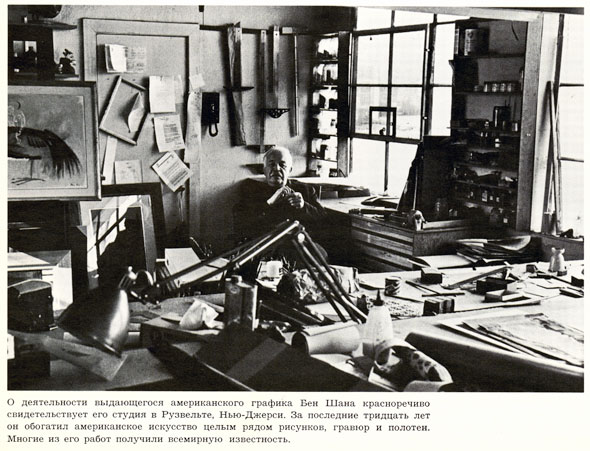 Black and white photo of a man sitting in his studio; many tools, such as lights and rulers are visible