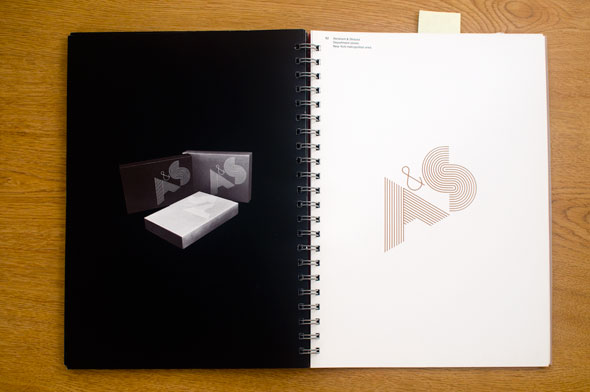 Spread; right is a diagonal graphic reading "A&S', it's made of many tiny lines; left is a black and white application of the logo on various boxes against a black background