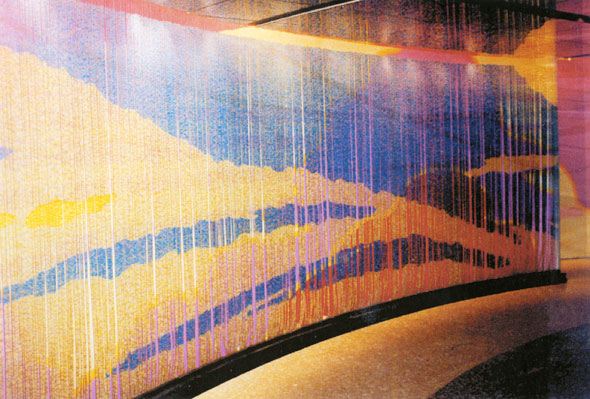 A photo the wall that covered by a curtain of beads. The wall can't be really seen but one can make out the red clouds and purple sky. The bead curtain shows a blue sky with light yellow clouds.