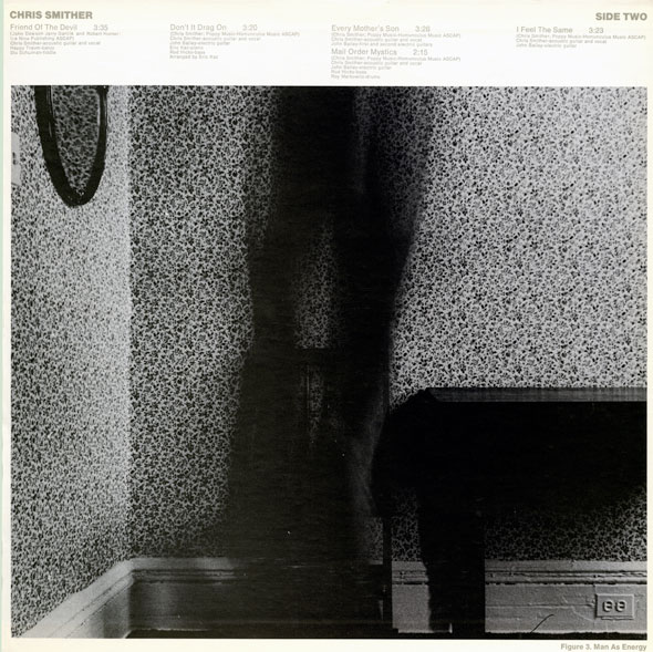 Black and white photo of a piano; next to it is a long dark smudge, a motion blur,  in a room with a floral designed wallpaper.