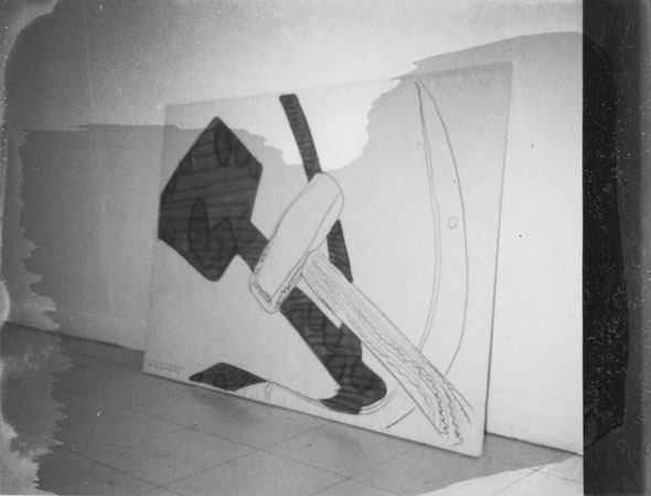 A photo of a huge canvas of a silkscreen of a mallet and a sickle. The canvas is on the floor supported by the wall. The photo has a smear in the middle making everything in that area slightly darker. 