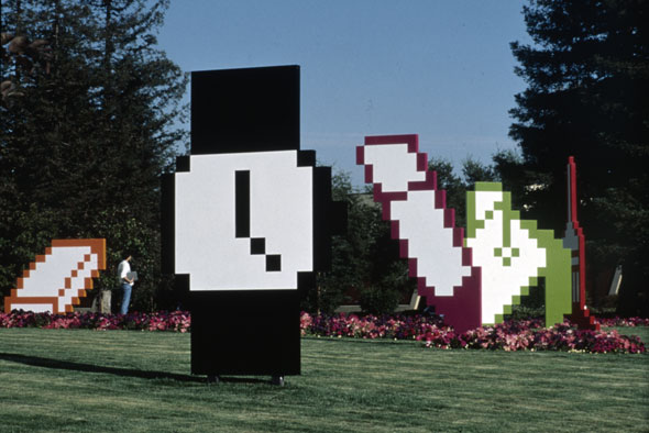 Environmental graphic design of pixelated watch, eraser, pencil, paint bucket, and paint brush on an open grass-field. 