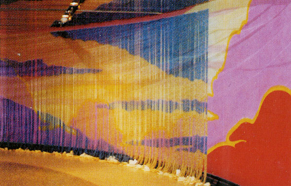 A photo the wall that is partially covered by a curtain of beads. The wall that is covered by the curtain can't be really seen but one can make out the red clouds and purple sky. The bead curtain shows a blue sky with light yellow clouds.