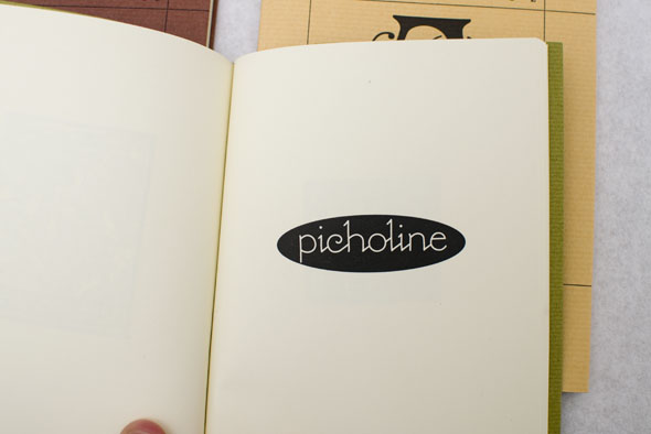 Green book opened to reveal a black and white logo reading "picholine" in a delicate font