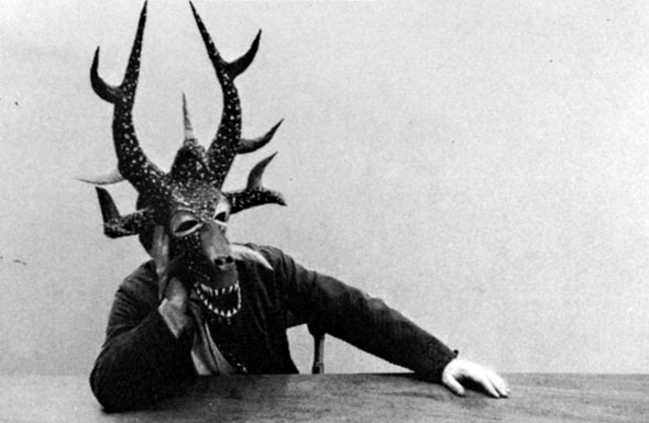 Black and white photograph of someone wearing a complex, dragon-like mask with large horns