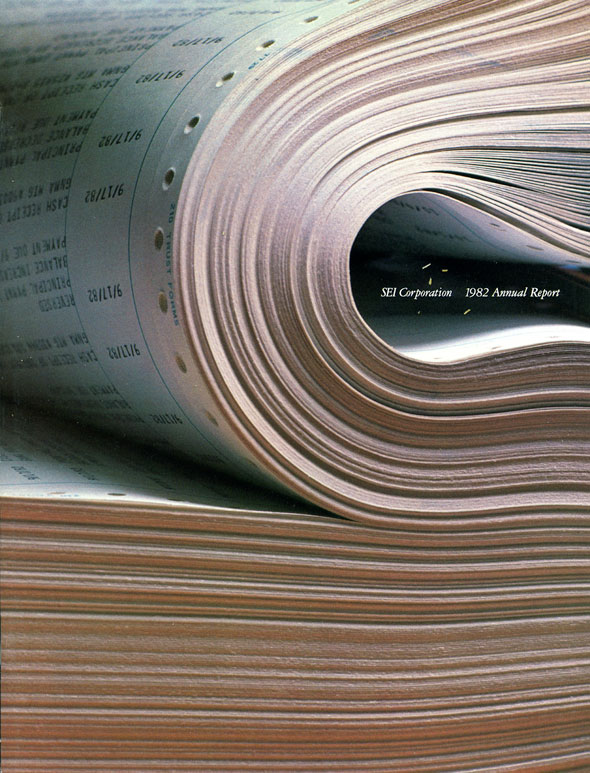 A photo of a bundle of paper. The top half of the bundle is folded over. Between the fold is "SEI Corporation. 1982 Annual Report" in white text. 