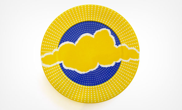 A colorful dining plate. The plate's center is a a bright blue and around is a sunny yellow. At the centre is a yellow cloud with a white outline, the cloud is big enough to touch the sides of the plate. There is a white polka dot design that spread out from the center of the plate. 
