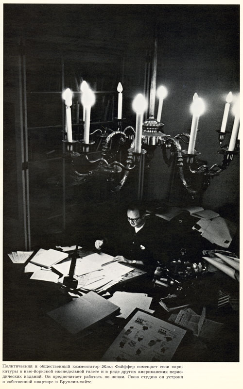 Dark, black and white photo of a man working at a desk covered in paper. The shot is from above, with the chandelier in the foreground. 