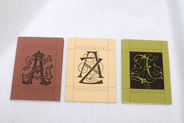 Three books with red, cream and green covers lined up on a white table. All have ornately designed covers with the letters A and Z