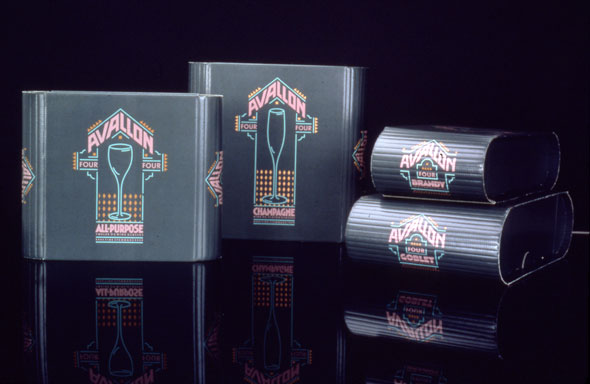 A photo of a product. There are four cardboard boxes. Two are standing up right on the left side the other two are stacked on right side. The upright boxes have similar design for "Avallon" The design is similar to a Las Vegas neon sign with the neon blue, pink, and yellow colors and the design of a blue wine glass with the Product name "Avallon" in neon oink grand text. The stacked boxes have a smaller version of that design without the wine glass. 