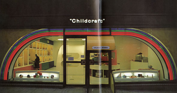 A photo of the "Childcraft" location from the outside. It has an large windows, so you can see inside. There is a illuminated circular motif near the windows that looks like a rainbow. The entrance door has a bright yellow storefront awning and near the door is a quarter circle wall walkway. "Childcraft" on the top of the location in a simple white illuminated sign. The lettering is minimalistic and is not in all caps. Inside you can see the brightly colored lobby that has cubbies on the wall and toys displayed in front of the window.