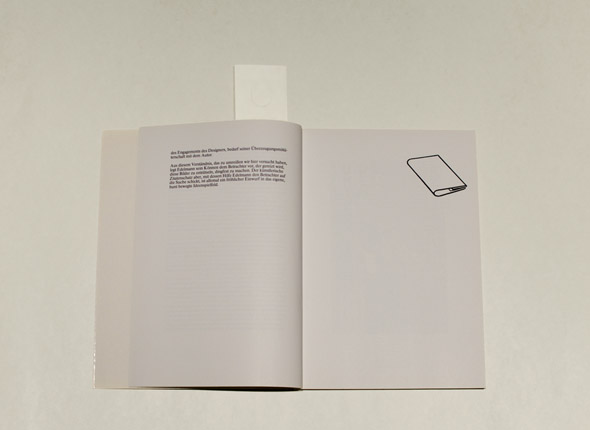 Open book on a white table; left page is mostly blank with a small block of text, right page has a graphic of a pamphlet