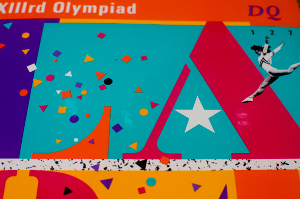 Closeup photo of a bright colorful magazine header; confetti-like shapes, a small black and white gymnast, a star and the letters LA are visible.