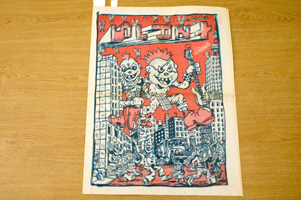 A front or back cover of a news paper. Two punk rock, grunge looking teens are giants. They step over buildings with people running away from them. The illustration has navy blue outlines and white and dull red shading. In the red sky the title of the News Paper, "Slant" is written is a way where every over letter is turned 90 degrees. 