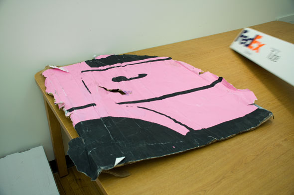 A photo of worn ripped piece of cardboard. The cardboard is with small black details of part of a car's door.