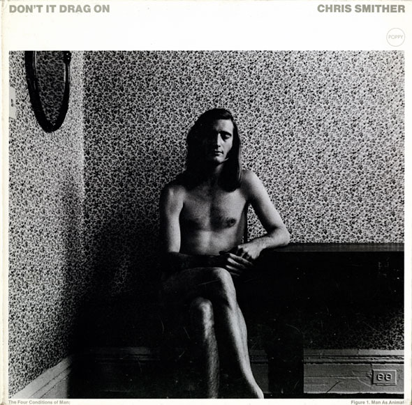 Black and white photo of a nude long-haired man sitting by a piano in a wallpapered room. His eyes are closed and a shadow is casted on half his face. A mirror is visible on the wall, which has a floral designed wallpaper.