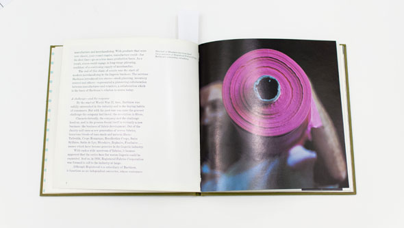 An opened book of a photo focused on a pink-purple roll of synthetic fabric, carried by a man's shoulder.