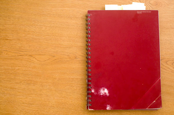 Color photo of a red spiral notebook on a wooden table.